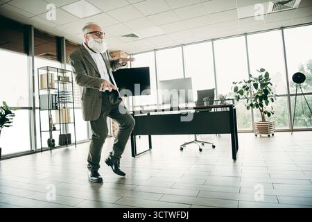 Homme d'affaires âgé dansant en toute confiance dans un espace de bureau moderne avec un blazer élégant et un comportement professionnel Banque D'Images