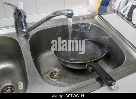 Une poêle chaude et bouillante immergée dans l'eau dans un évier de cuisine. Une poêle qui n'a pas refroidi sous l'eau froide Banque D'Images