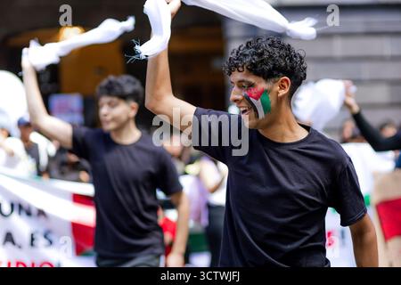 Un jeune manifestant souriant avec le drapeau palestinien peint sur son visage agite un tissu blanc lors d'une manifestation à Puebla. Banque D'Images