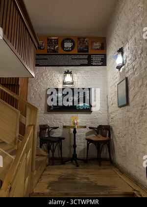 L'image montre un petit coin salon dans Kitabeyi Cafe avec deux chaises en bois et une table ronde en métal contre un mur de briques blanches. Un tableau noir avec cha Banque D'Images
