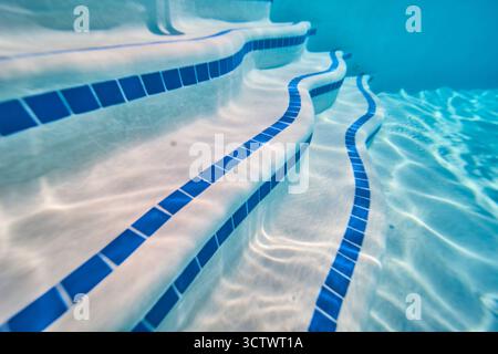 Marches de piscine sous-marine avec carreaux bleus et motifs de lumière du soleil dans le cadre du quartier Banque D'Images