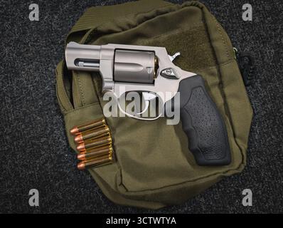 Revolver compact en acier inoxydable avec munitions sur une pochette tactique verte. Arme de transport dissimulée pour l'auto-défense personnelle. Banque D'Images