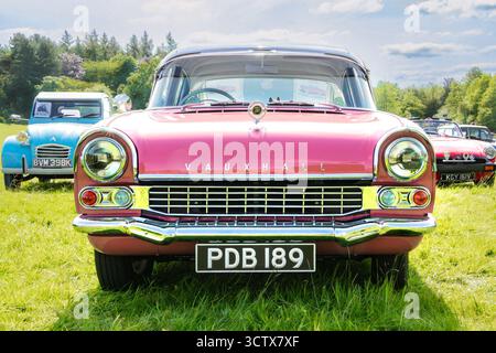 Voiture vintage vauxhall cresta classique rose et blanc exposée à un salon automobile sur un terrain herbeux avec des gens admirant des véhicules en arrière-plan Banque D'Images