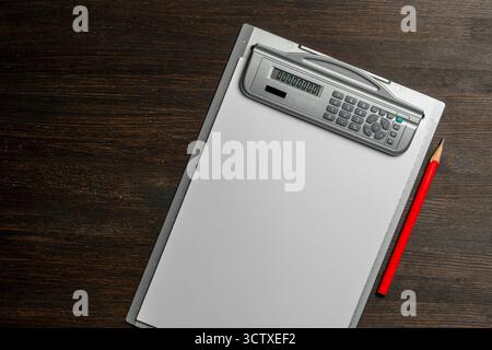 Presse-papiers avec un papier blanc vierge et un crayon rouge sur une table en bois, gros plan, vue de dessus. Bureau gris avec calculatrice électronique et règle Banque D'Images
