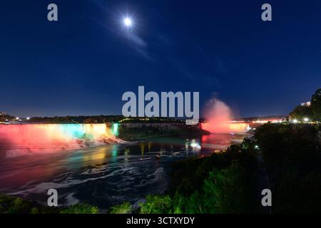 Une vue nocturne spectaculaire sur les chutes du Niagara avec les chutes canadiennes en fer à cheval et les chutes américaines illuminées par des feux d'artifice vibrants. Banque D'Images