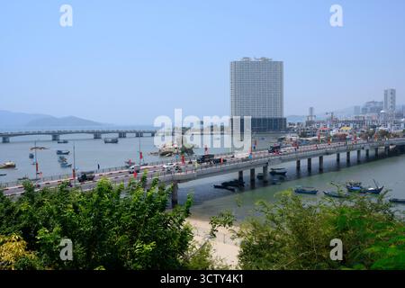 NHA TRANG, VIETNAM - 25 AVRIL 2025. Vue sur la ville avec un pont sur la rivière Cai, gratte-ciel et bateaux de pêche Banque D'Images