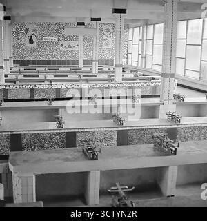 La salle vide d'un nouveau marché soviétique à Sloviansk, RSS d'Ukraine, est prête pour les affaires dans cette photo en noir et blanc de 1970. Les rangées de compteurs carrelés sont entièrement équipées de balances mécaniques vintage identiques, créant un motif graphique fort. L'intérieur moderniste présente de grandes fenêtres et des murs décoratifs en mosaïque ornés de motifs floraux et végétaux sous un panneau indiquant « Ovoschi » (légumes). Cette image capture l'état propre et ordonné d'un espace commercial public juste avant son ouverture, symbolisant le commerce planifié de l'URSS Banque D'Images