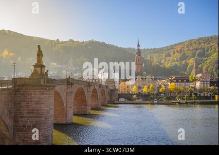 Le coucher du soleil jette une lueur chaude sur la paisible rivière Neckar, mettant en valeur le charme et l'histoire de Heidelberg. Banque D'Images