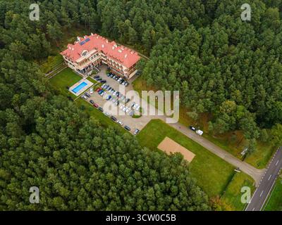 Prise de vue aérienne de l'hôtel Drohicki par drone, montrant l'architecture détaillée du toit et un parking organisé entouré d'une forêt dense Banque D'Images