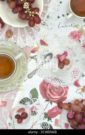 Thé anglais à cinq heures avec décorations roses, serviettes rétro, fleurs, fruits et dessert. Perles et raisins. Banque D'Images
