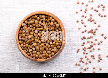 Lentilles brunes cuites, dans un bol en bois, sur du lin. Petites lentilles brunes en conserve, lentilles de montagne non décortiquées, graines de Lens culinaris. Banque D'Images