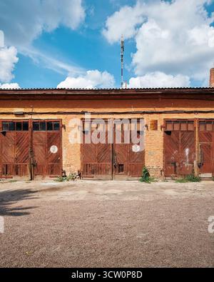 Ancien bâtiment utilitaire d'usine avec trois portes de garage - grange ou hangar. Bloc de garages en brique avec portes en bois brun. Banque D'Images