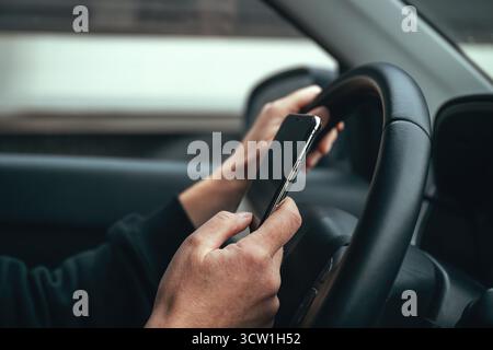 Conducteur irresponsable utilisant un téléphone portable tout en conduisant dans les rues de la ville. Mise au point sélective. Banque D'Images
