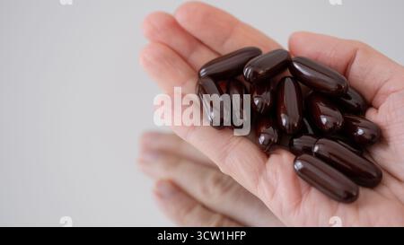 Gros plan de mains tenant un tas de capsules molles brunes sur un fond neutre. Concept de vitamines, suppléments et soins de santé naturels. Parfait Banque D'Images
