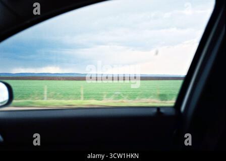Photo analogique de 35 mm depuis le siège passager, regardant sur un champ vert avec la montagne Fruška Gora à l'horizon. Scène rurale calme et spacieuse. Banque D'Images