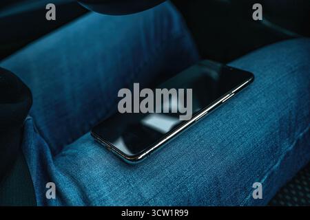 Pilote femme portant un Jean tenant un smartphone sur ses genoux tout en étant assise dans la voiture. Mise au point sélective. Banque D'Images