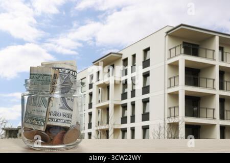Pot avec des dollars et des pièces contre condominium. Économiser de l'argent pour acheter appartement Banque D'Images