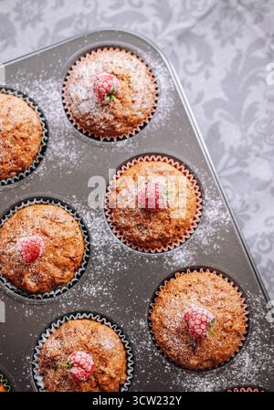 Plat vue aérienne de délicieux muffins faits maison dans des gobelets en papier sur une table surmontée de framboises biologiques fraîches Banque D'Images