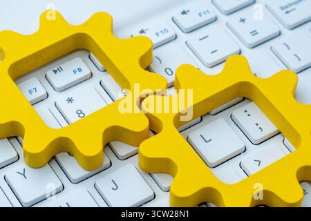 Formes d'engrenage jaunes sur un clavier d'ordinateur symbolisant l'automatisation dans les systèmes informatiques, le flux de travail numérique et l'intégration de processus technologiques. Banque D'Images