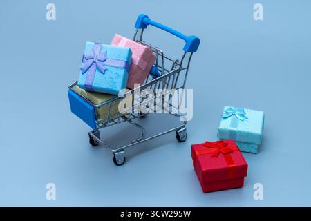 Mini panier rempli de boîtes cadeaux colorées sur fond bleu. Achat en ligne, vente au détail, ventes de vacances et concept d'achat de consommateurs. Banque D'Images