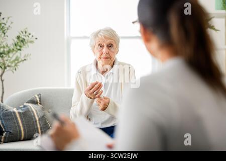 Une vieille femme pensant avec le psychologue dans le bureau de consultation pour l'esprit, l'évaluation ou l'évaluation. Banque D'Images