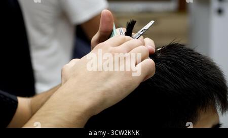 Un homme se faisant couper les cheveux par un barbier dans un salon de coiffure animé de style vintage. Banque D'Images