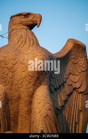 Sculpture de l'aigle Arlington Memorial Bridge Washington DC // WASHINGTON DC — une sculpture d'aigle, l'une des deux statues de granit, est située à l'extrémité ouest du pont commémoratif d'Arlington. Cette image montre la sculpture sur le côté sud de la chaussée, orientée vers le sud. Dessinés par Carl Paul Jennewein et sculptés par les frères Piccirilli, les aigles ont été installés en 1932. La sculpture est illuminée par les rayons dorés du soleil couchant. Banque D'Images