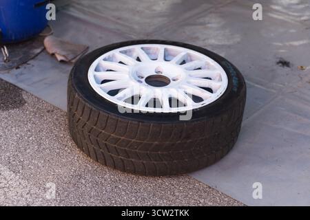 Pneu performance à profil bas avec jante en alliage blanc à rayons multiples repose sur un plancher d'atelier. Banque D'Images