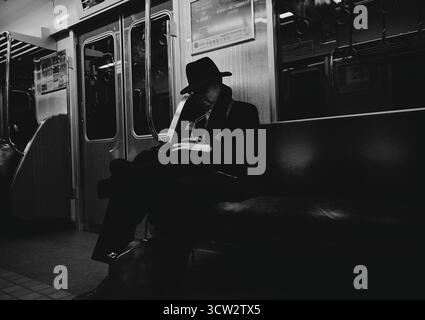 Un homme en costume sombre et chapeau repose tranquillement sur un train de métro d'Osaka en noir et blanc Banque D'Images