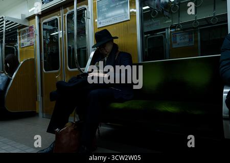 Homme aîné dans un costume sombre et chapeau repose tranquillement sur un train de métro Osaka Banque D'Images