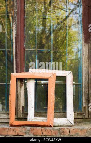 Deux vieux cadres en bois sont assis sur un rebord de fenêtre en brique devant une fenêtre à plusieurs vitres altérées, évoquant un sens de l'histoire et de la décadence artistique. Banque D'Images