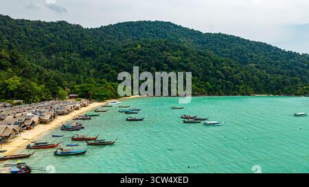 Une vue aérienne imprenable sur un village balnéaire tropical avec des rangées de petites cabanes le long du littoral, les bateaux de pêche traditionnels sont ancrés dans le turquois Banque D'Images