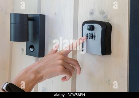 Personne entrant le code dans le coffret à clés extérieur. Gros plan d'une main saisissant des chiffres sur un coffret à clés à combinaison mural à côté d'une lumière de sécurité allumée Banque D'Images