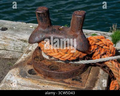 Borne d'amarrage rouillée avec corde orange sur le quai en bois à côté de l'eau Banque D'Images
