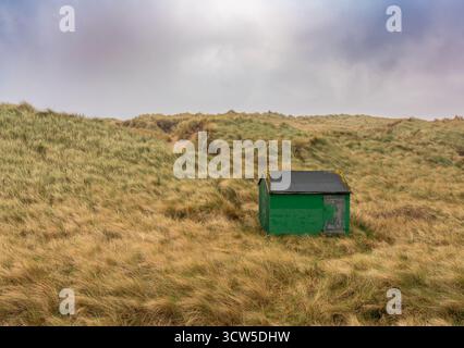 La cabane de pêcheur verte altérée se trouve parmi les hautes herbes dunes côtières Banque D'Images