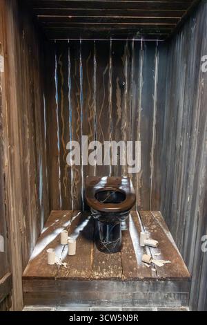 Toilettes en bois ouvertes avec des murs de planches et des résidus de papier toilette sur le sol Banque D'Images