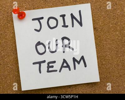 Un billet autocollant avec les mots « Join our team » au marqueur noir, attaché à un panneau d'affichage en liège avec une punaise rouge. Cette image représente le recrutement, Banque D'Images