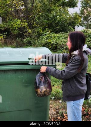 Une femme jette un sac de déchets dans une poubelle. Élimination des déchets à l'extérieur. Banque D'Images