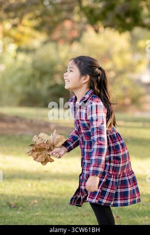 Smiling Girl court avec des feuilles un jour d'automne Banque D'Images