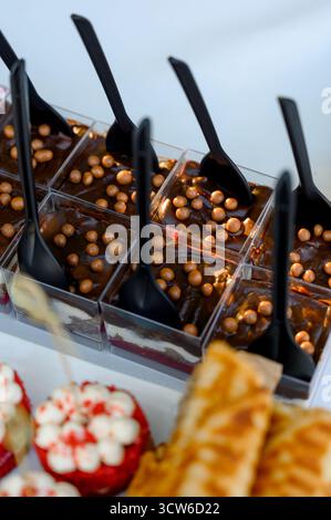 Mini desserts en cubes de verre transparent avec cuillères en plastique noir.gros plan de desserts en couches de chocolat et de baies pour la restauration ou les célébrations Banque D'Images