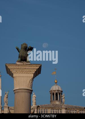 Colonne du lion de Saint-Marc et lune de jour - vue rapprochée emblématique et détaillée du lion ailé de Venise au sommet de sa colonne sur la Piazzetta San Marco, avec le visib Banque D'Images