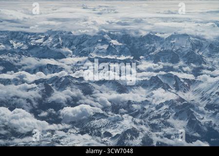 Alpes et nuages enneigés spectaculaires - vue aérienne époustouflante capturant les pics montagneux accidentés et enneigés des Alpes, émergeant d'une épaisse laye Banque D'Images