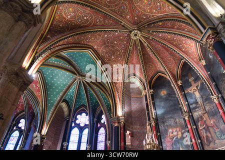 Voûtes gothiques et peintures murales de Sainte-Chapelle - vue en bas angle d'une voûte gothique richement peinte en rouge, or et sarcelle, à côté d'un grand crucifixi Banque D'Images