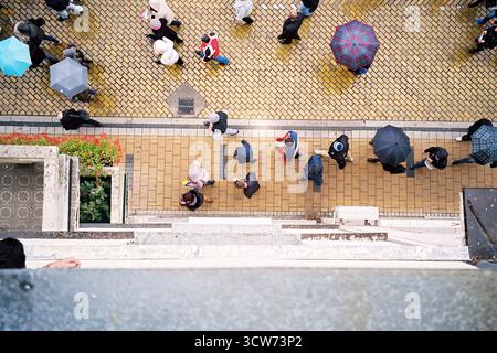 Plan vertical à grand angle de personnes revenant d'un rassemblement, certaines avec des parapluies, marchant sur un chemin lisse en briques jaunes de clinker. Banque D'Images