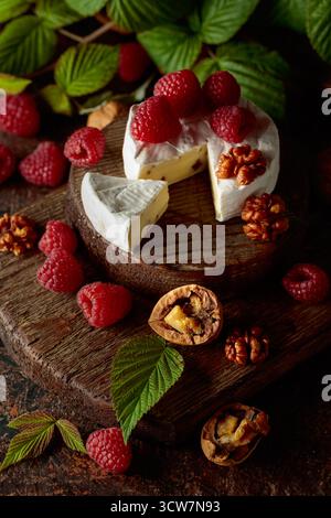 Camembert avec framboises fraîches et noix sur une table vintage brune. Banque D'Images