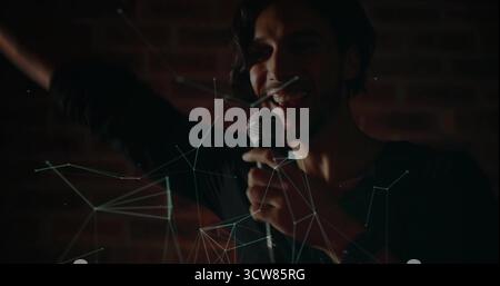 Chanteur en chemise sombre chantant passionnément dans le micro à main sur la scène de bar, lignes réseau. Performance, musique, concert, vie nocturne, artistique, Banque D'Images