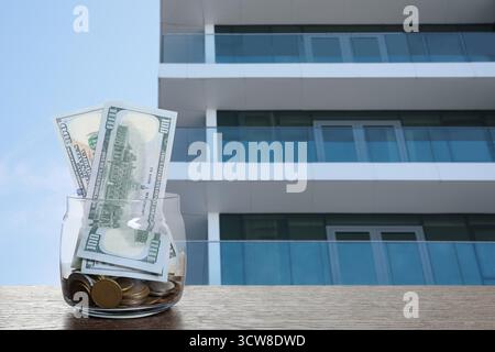 Pot avec des dollars et des pièces contre condominium. Économiser de l'argent pour acheter appartement Banque D'Images
