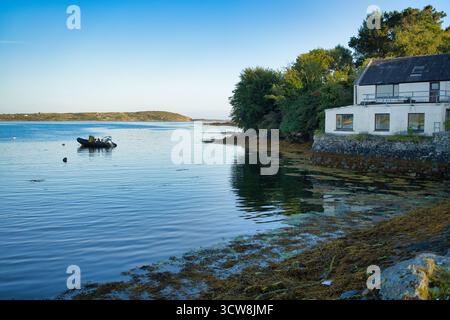 Une scène côtière sereine en Irlande avec une maison au bord de l'eau et un bateau. Banque D'Images