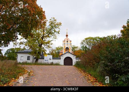 Un sentier couvert de feuilles d'automne tombées mène à la porte d'entrée et au clocher jaune d'une église historique, entouré d'arbres colorés Banque D'Images