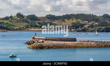 Détail du brise-lames en pierre du port de Cudillero, avec la balise de navigation et de petits bateaux ancrés dans la baie. La côte asturienne s'étend wi Banque D'Images